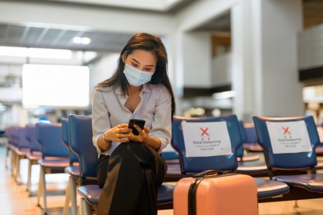 A young lady is waiting at the airport for her flight while wearing mask