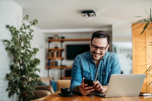 A young man sending a text message while working from home