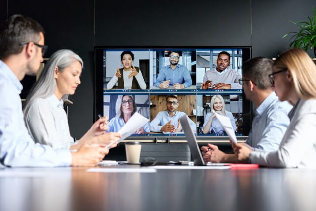Global corporation online videoconference in meeting room with diverse people sitting in modern office discussing evolving business processees