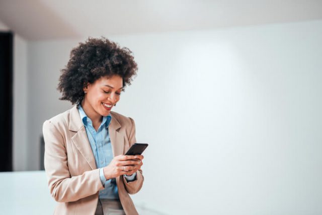 Beautiful smiling curly-haired businesswoman using smartphone