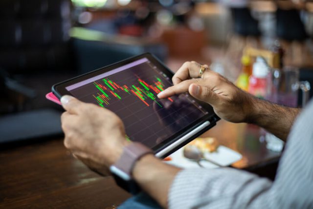 big data image in which Asian business men using a tablet for working and checking stock trends chart and financial analysis at coffee shop