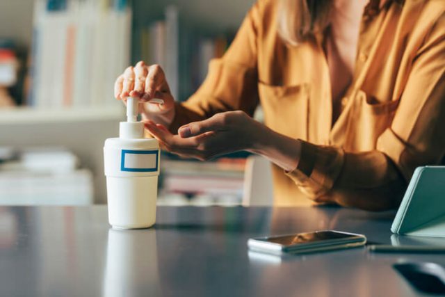 Close up photo of woman washing hands with alcohol gel while sitting at her desk.