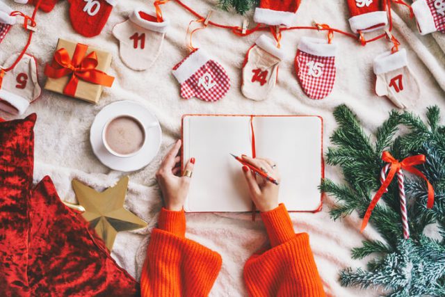 Woman writing a Christmas decor to do list in a notebook.