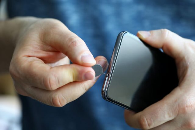Male hands getting sim card slot of his smartphone out closeup