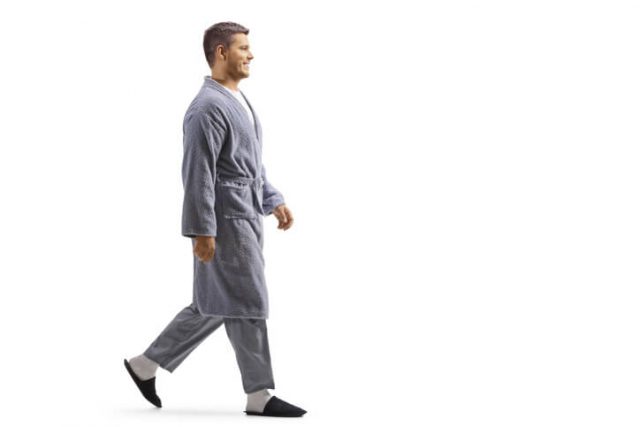 Full length profile shot of a young man wearing a robe and walking isolated on white background as traveling essentials 