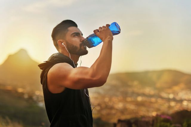 Shot of a young man exercising outdoors driking water as travel essentials 