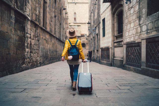 Young woman with suitcase walking at the street in Barcelona traveling essentials concepts