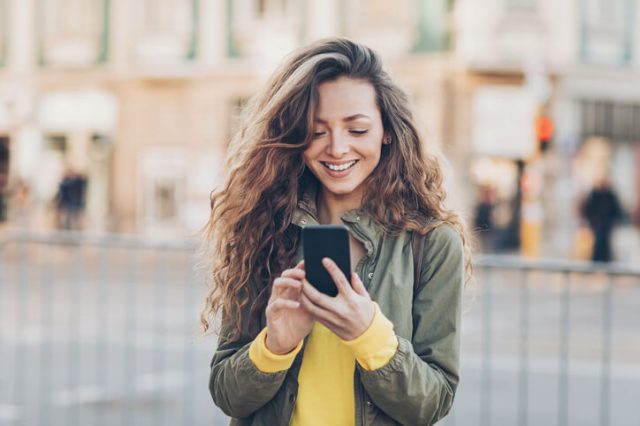 Young woman with smart phone texting outdoors in the city calling their loved ones and happy to save money calling