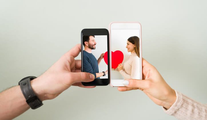 Close up of couple joining two smartphones together with a photo of an attractive man and young woman in love holding a red heart. Love concept in long distance relationship