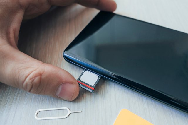 SIM card and microSD card tray with removal tool at the side of smartphone on a wooden table. free space for design and text