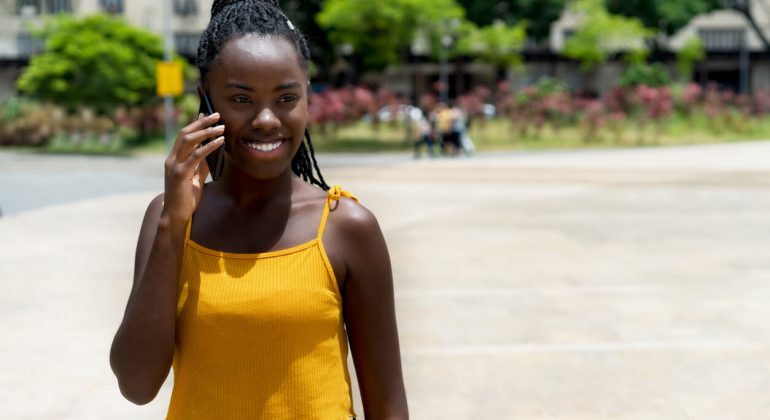 young adult calling nigeria and laughing at phone outdoor in summer in city